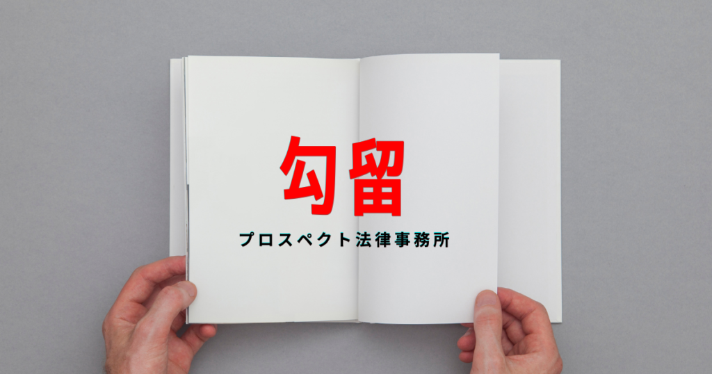 警察署の面会室を連想させる室内で、机の上の書類と時計を前に座る人物の手元
